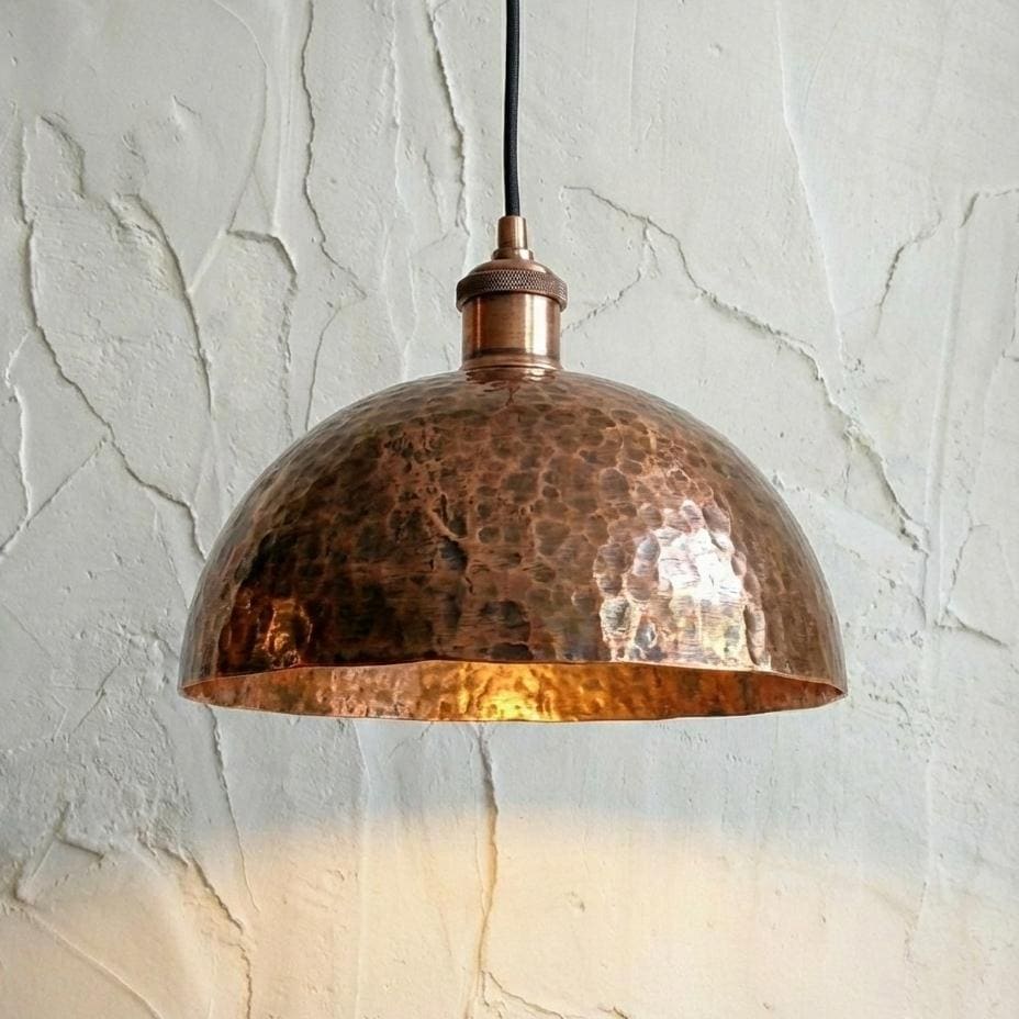 Copper pendant light hanging against a textured white wall