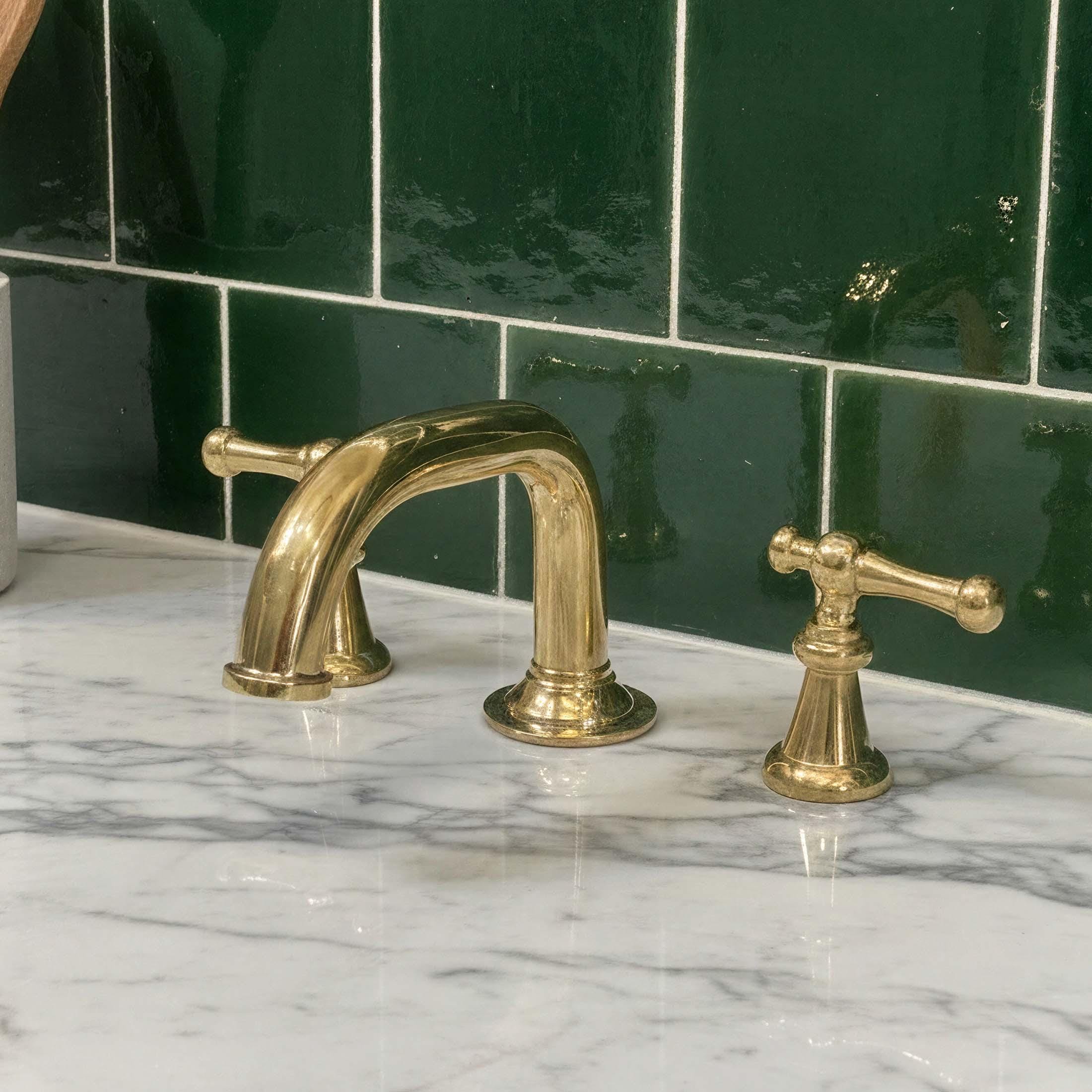 Gold faucet and handles on a marble countertop with green tiled wall in the background