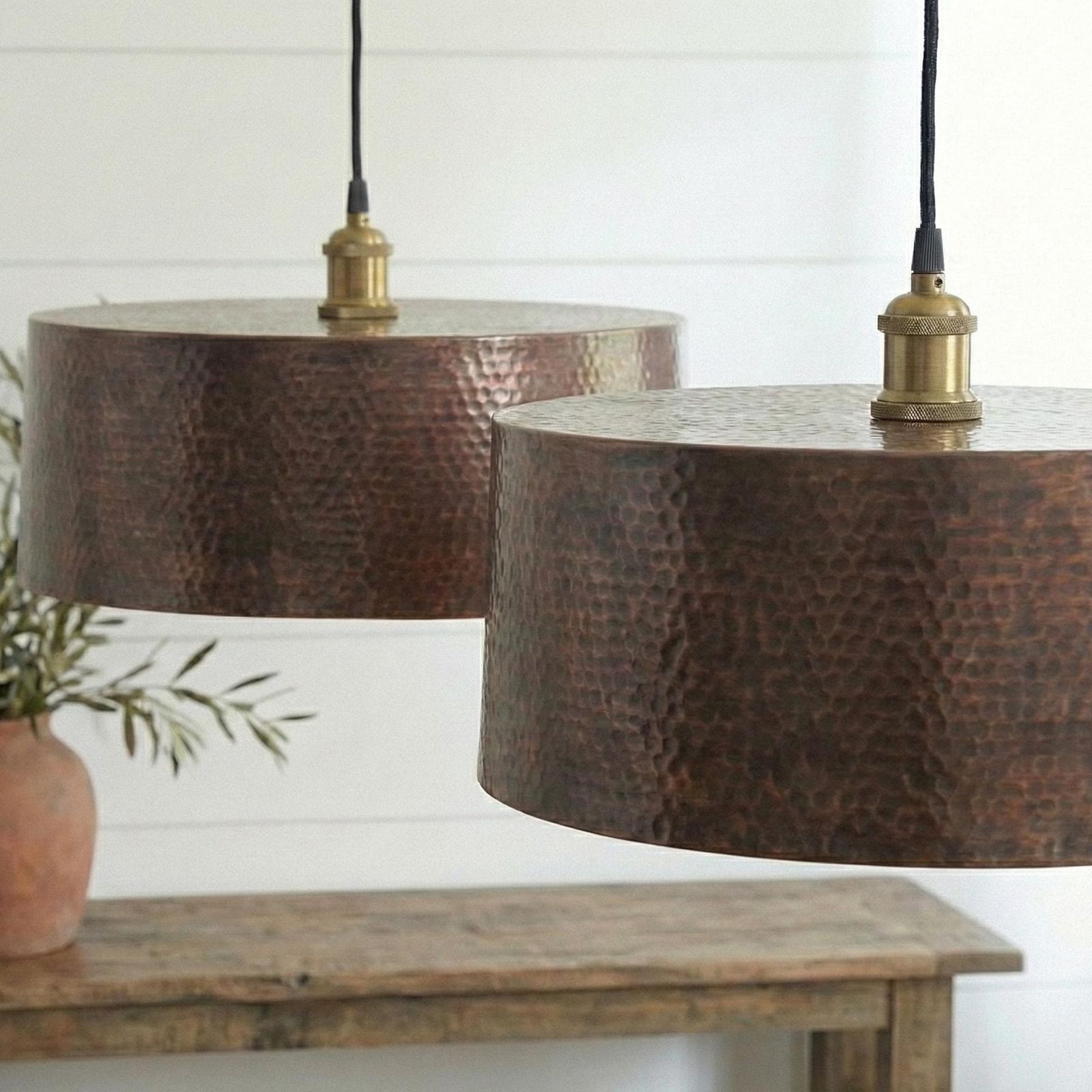Two copper pendant lights hanging above a wooden table with a white wall background.