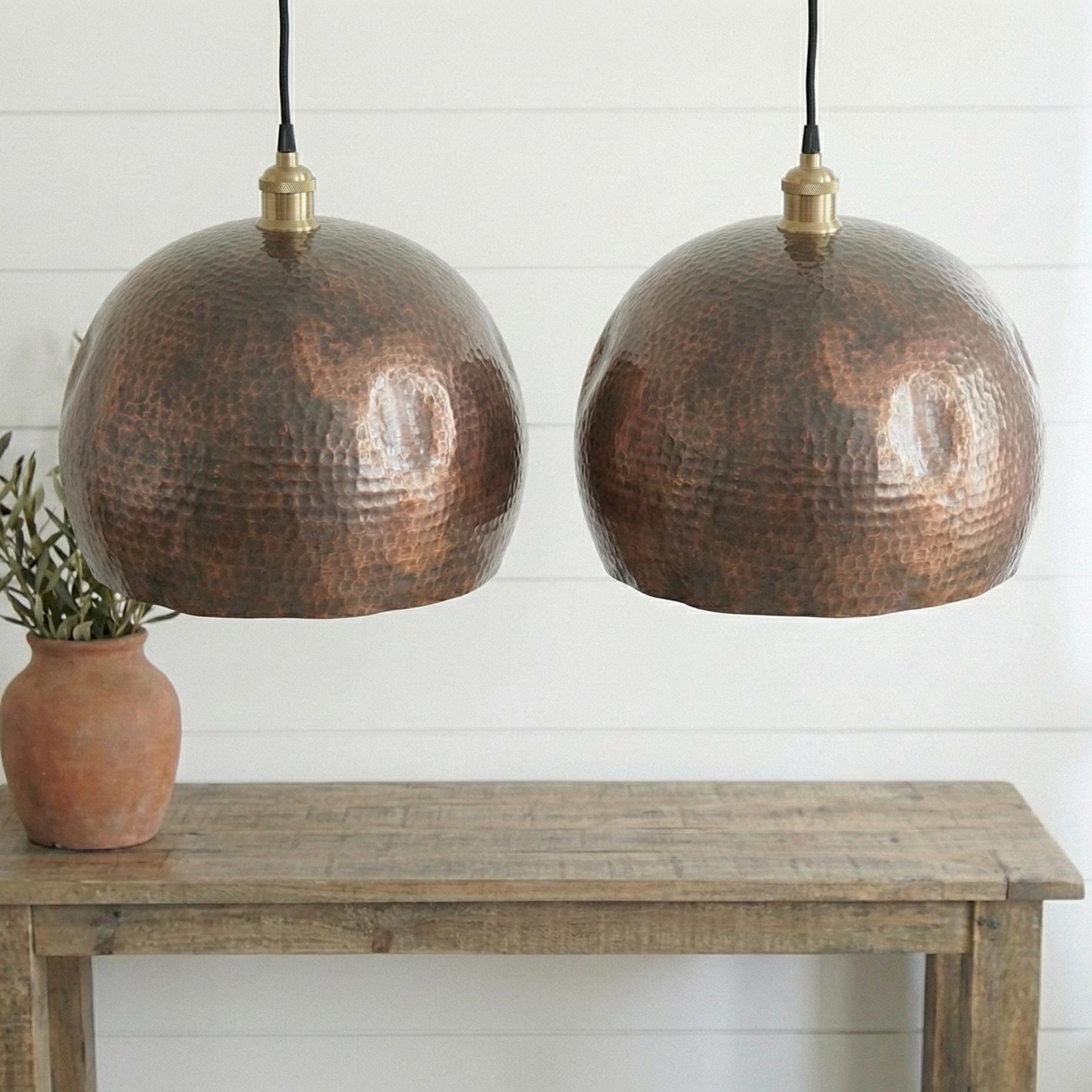 Two copper pendant lights hanging above a wooden table with a white wall background.