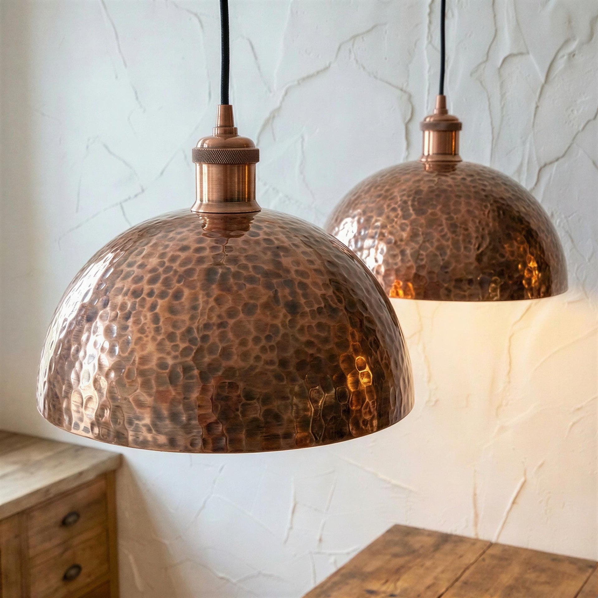 Two copper pendant lights hanging against a textured white wall.