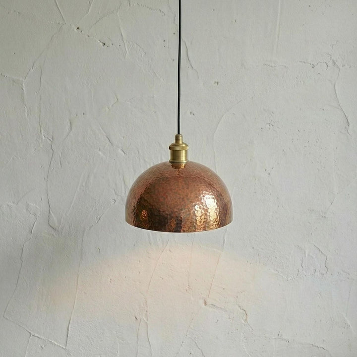 Copper pendant light hanging against a textured white wall