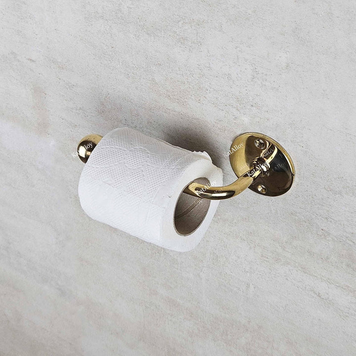 Gold toilet paper holder with a roll of white toilet paper on a light gray wall.
