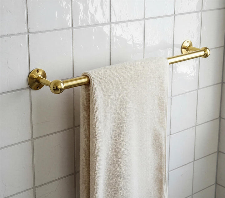 Gold towel rack with a beige towel on a tiled bathroom wall