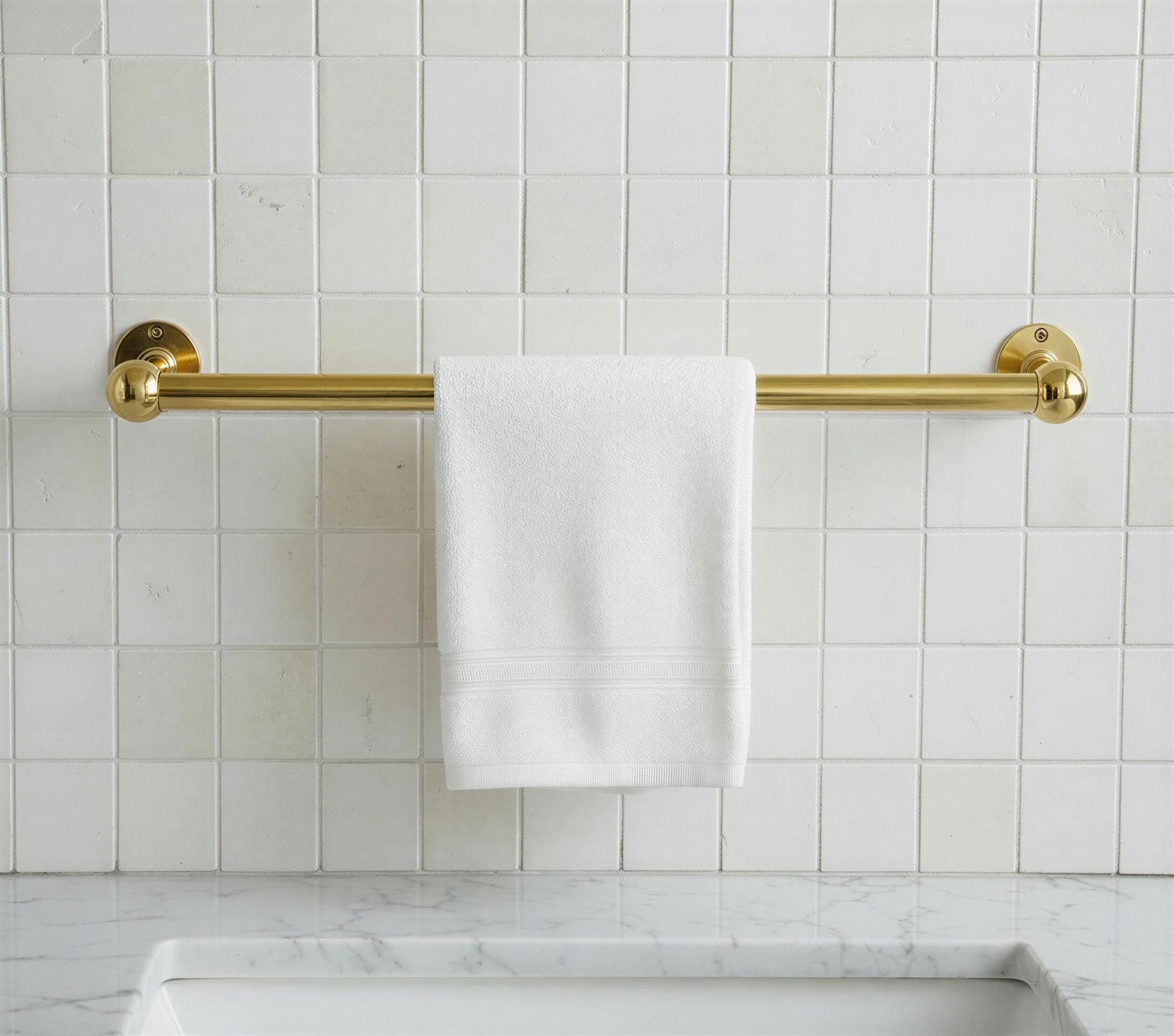 Gold towel rack with a white towel on a tiled bathroom wall.