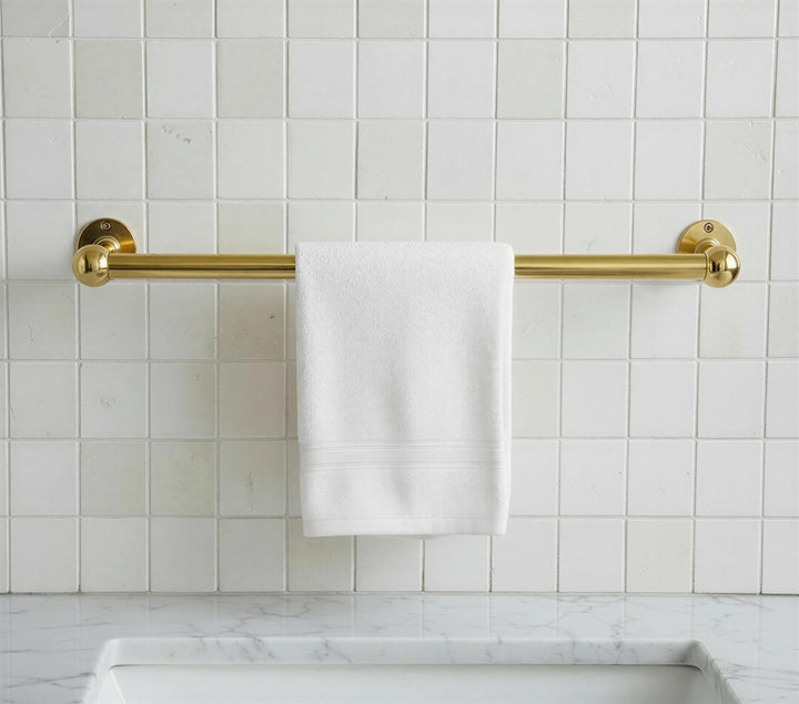 Gold towel rack with a white towel on a tiled bathroom wall.