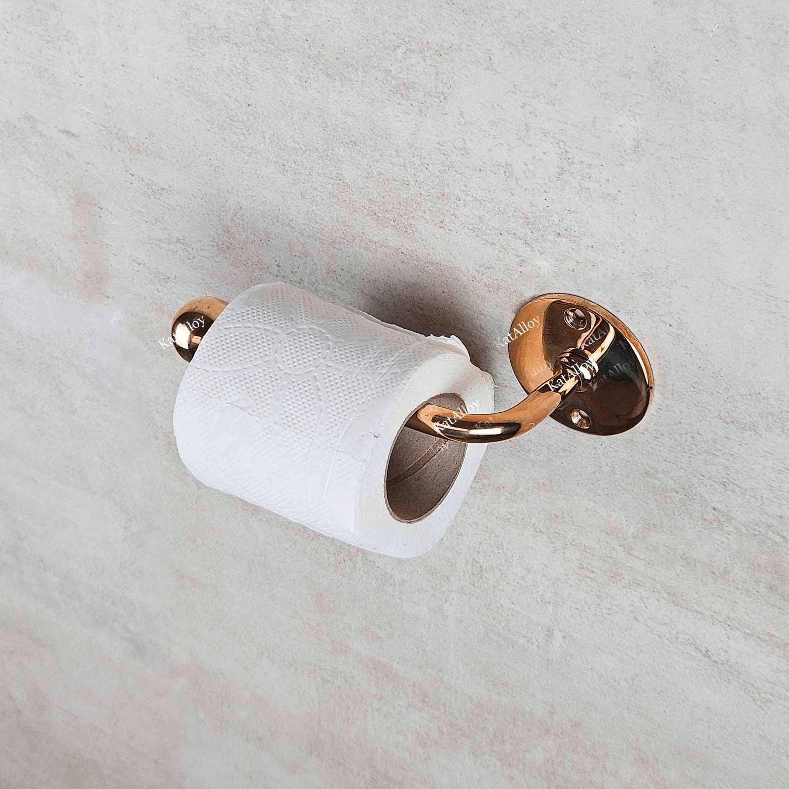Rose gold toilet paper holder with a roll of toilet paper on a marble wall.