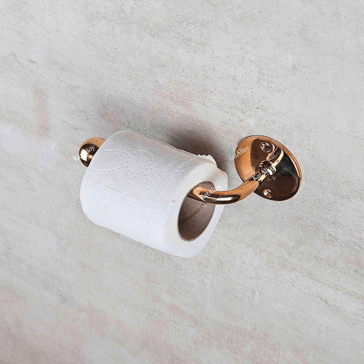 Rose gold toilet paper holder with a roll of toilet paper on a marble wall.