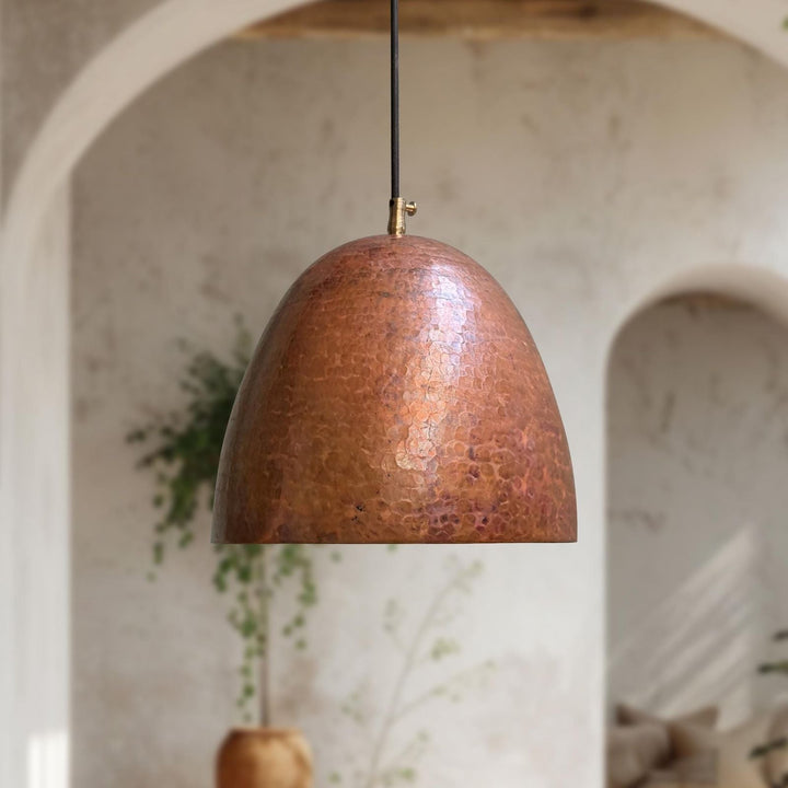 Copper pendant light hanging in a room with arches and plants