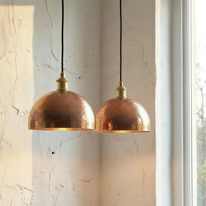 Two copper pendant lights hanging against a textured wall.