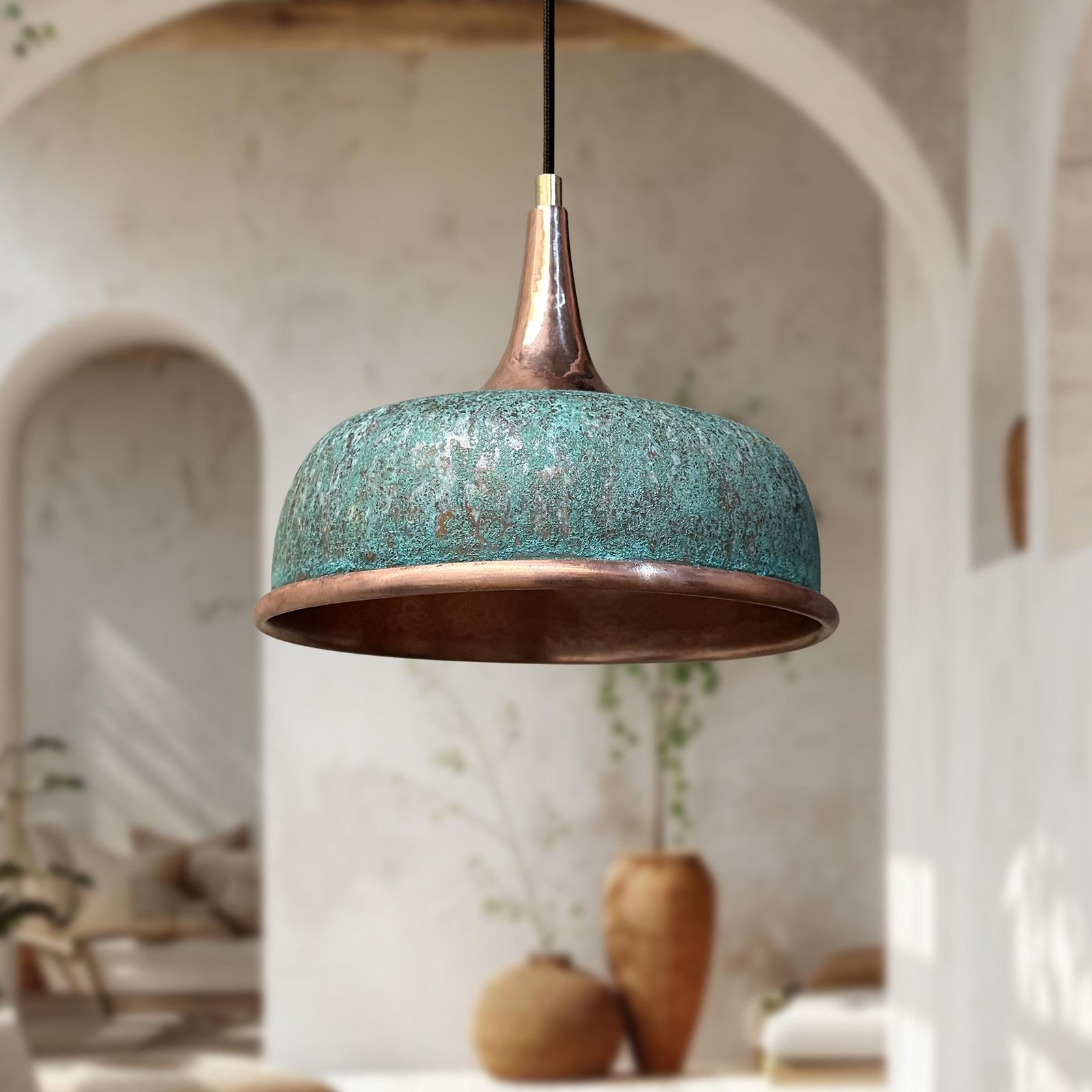 A dome-shaped pendant light with a distressed turquoise-blue enamel finish and a copper-toned metal rim and top, hanging in a softly blurred rustic interior with arches and neutral decor.