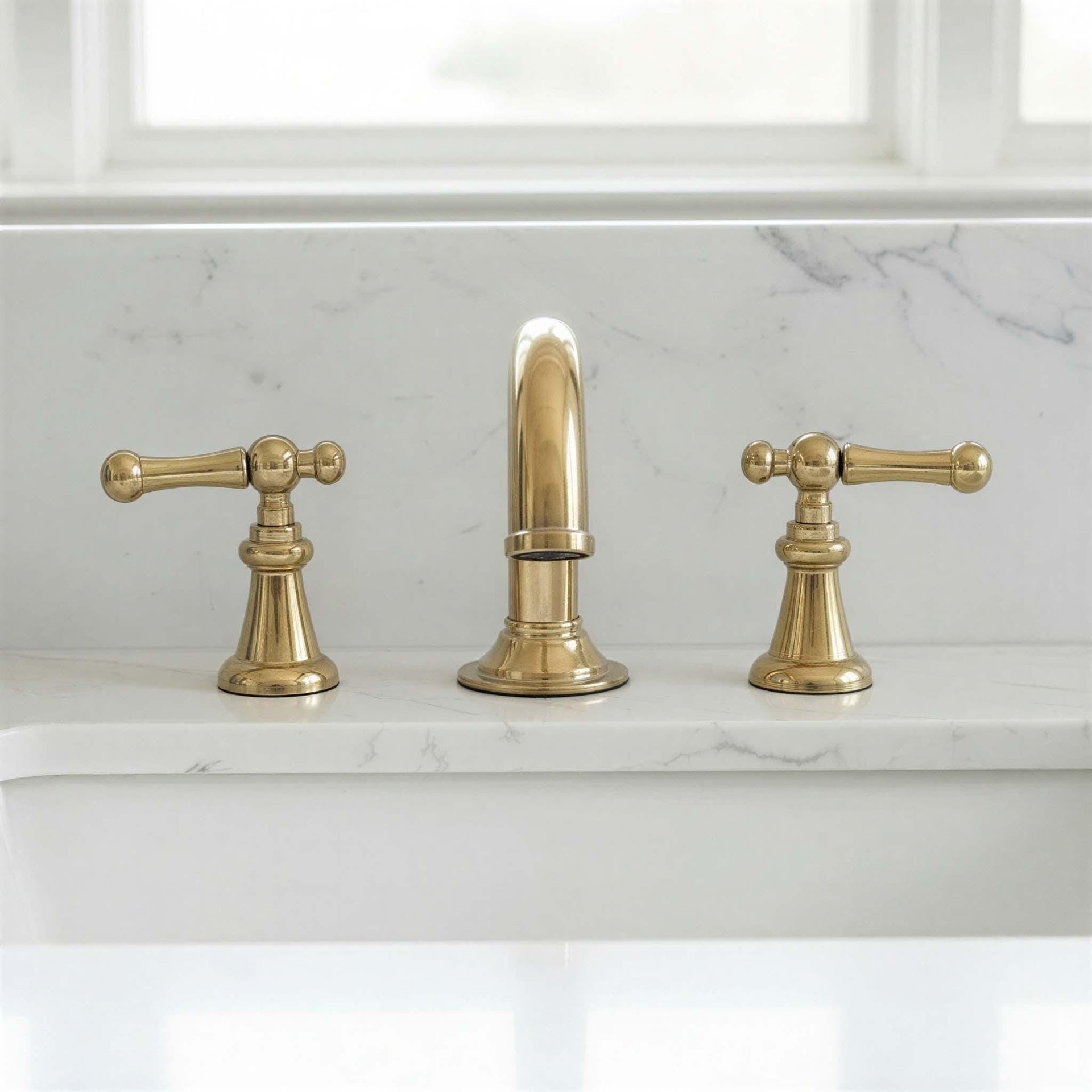 Brass faucet set on a marble countertop with a window in the background