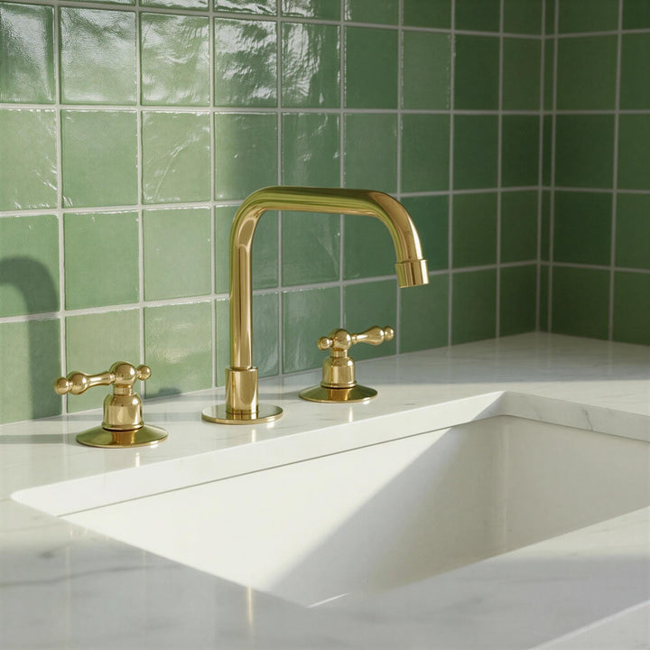 Gold faucet and handles on a white sink with green tiled wall