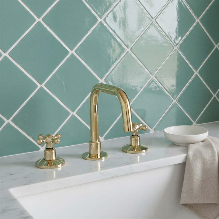 Gold faucet and handles on a white sink with green tiled wall