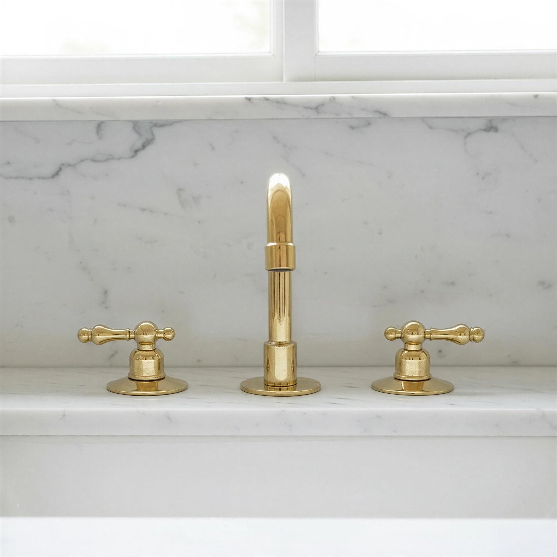 Gold faucet set on a marble countertop with a window in the background