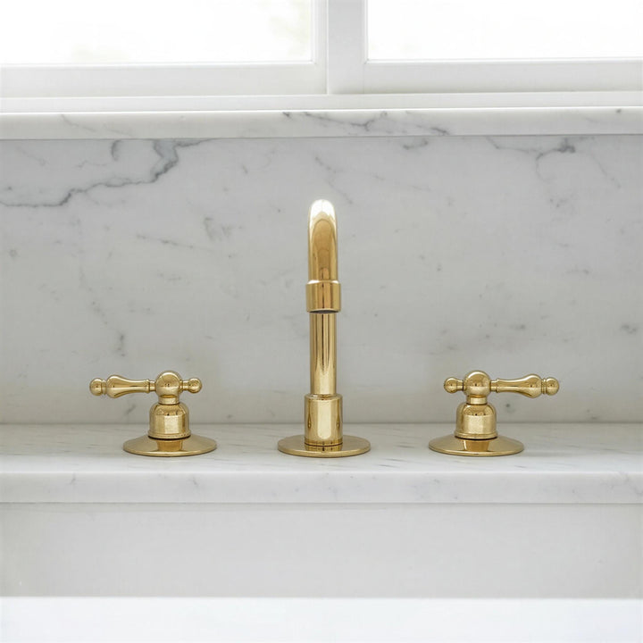 Gold faucet set on a marble countertop with a window in the background