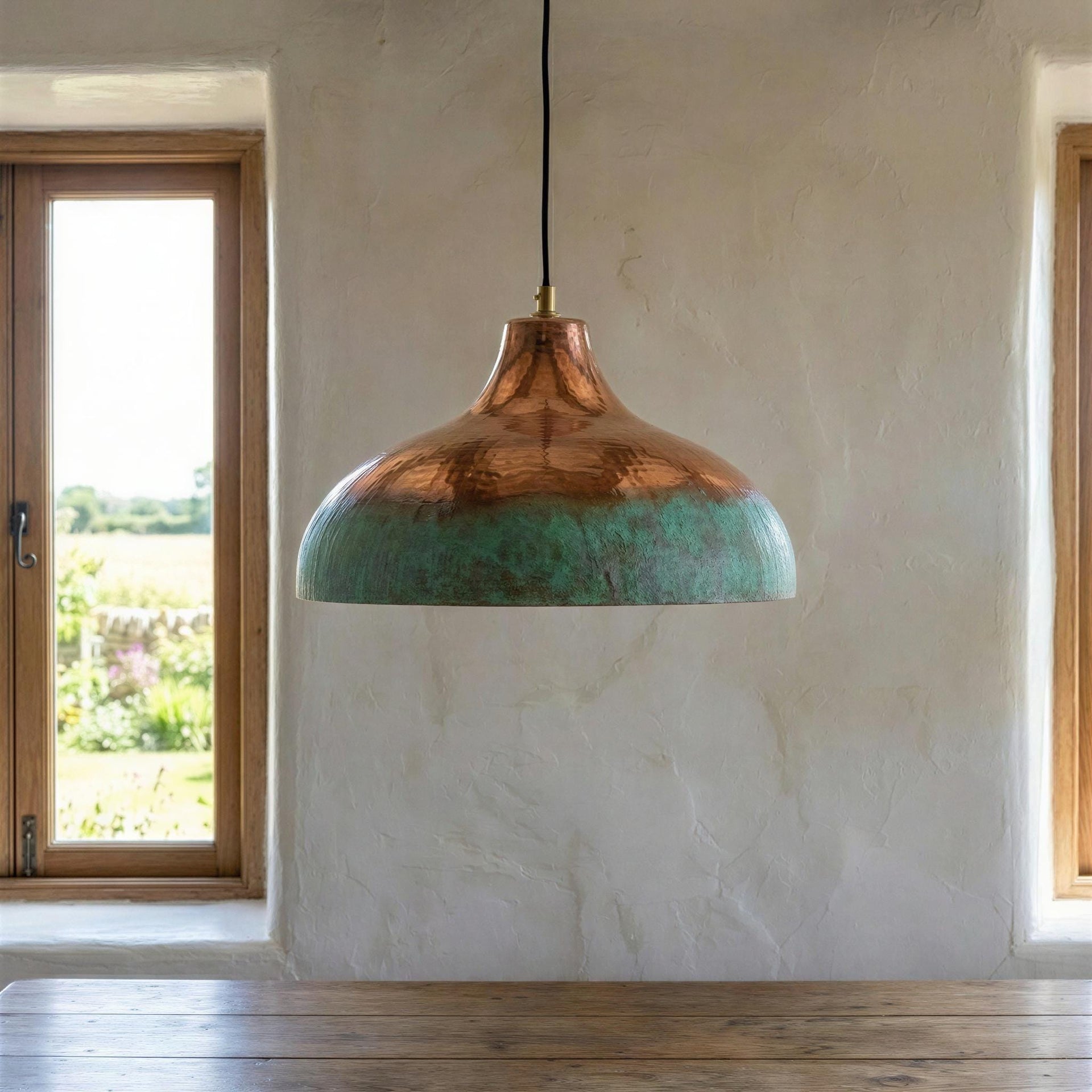 Copper pendant light with greenish-blue interior hanging in a room with a window and wooden floor.