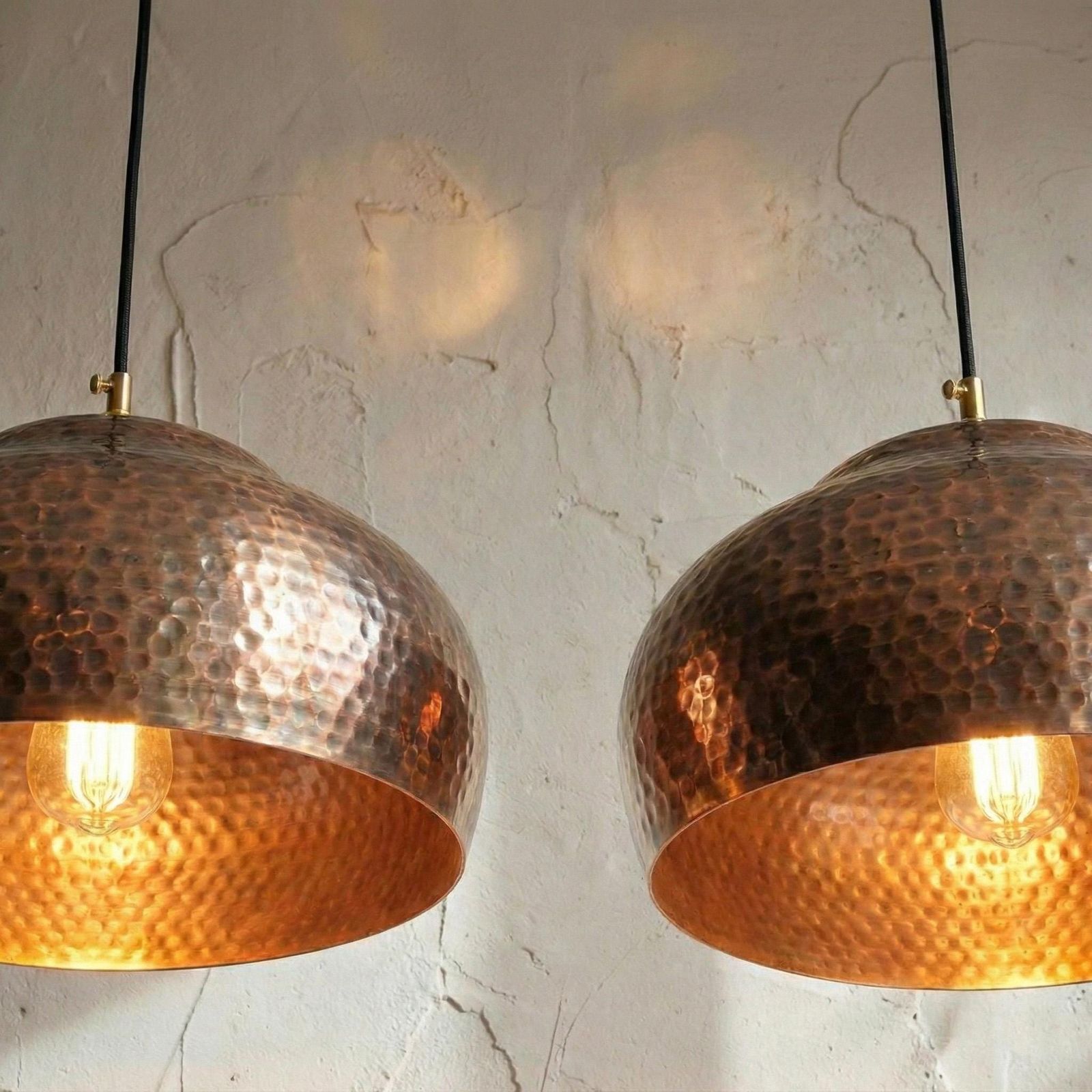 Two copper pendant lights hanging against a textured wall.