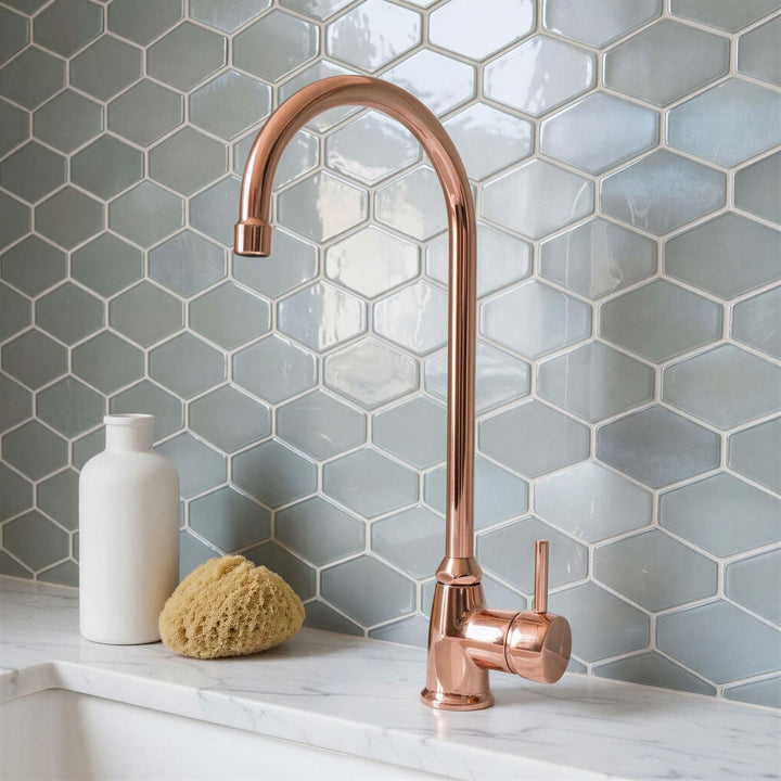 Rose gold faucet on a kitchen sink with hexagonal tiled wall