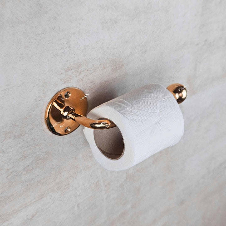 Rose gold toilet paper holder with a roll of toilet paper on a marble wall.