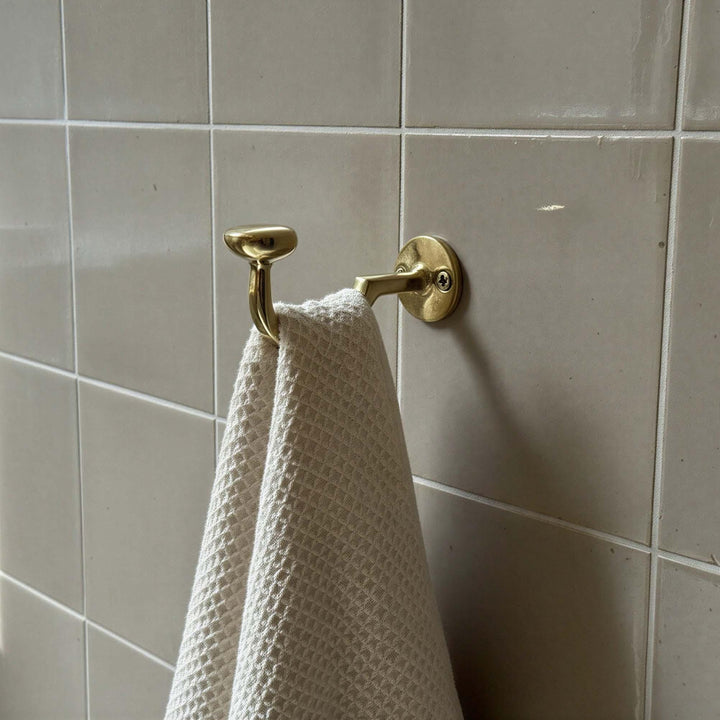 Gold towel hook with a white towel on a tiled bathroom wall