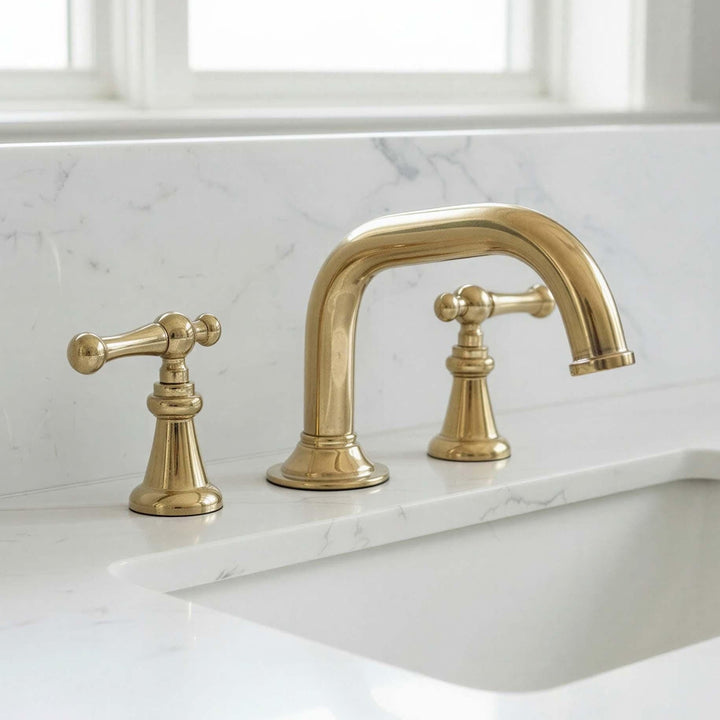 Gold faucet set on a marble countertop with a window in the background