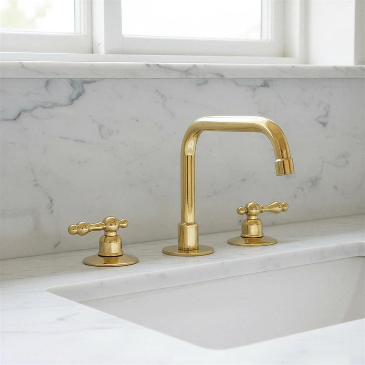 Gold faucet set on a marble countertop with a window in the background