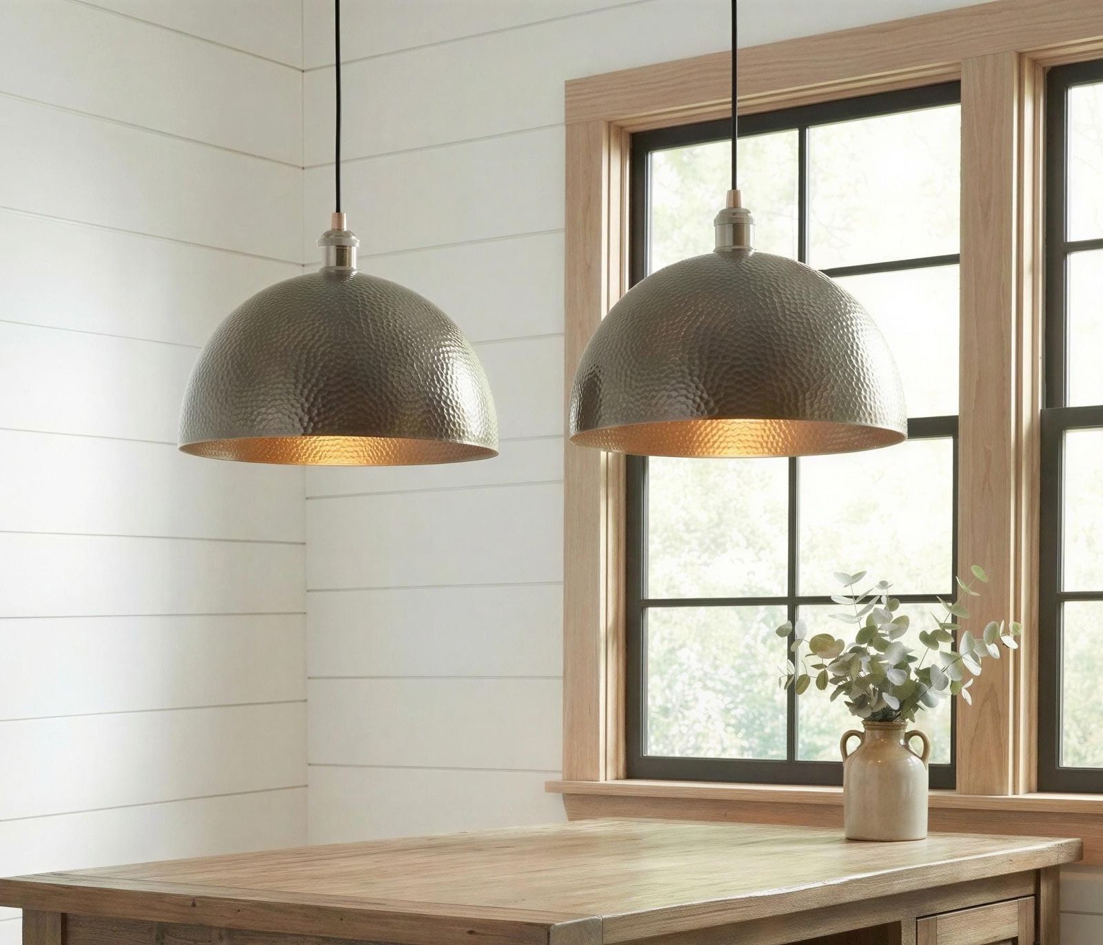 Two metallic pendant lights hanging above a wooden table with a window in the background.