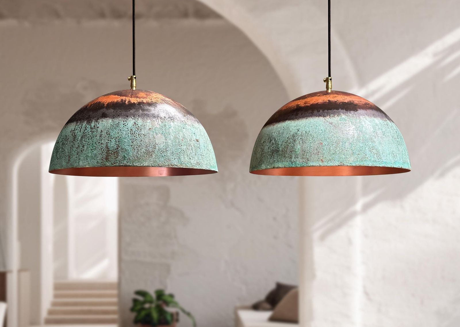 Two copper pendant lights hanging in a room with white walls and a plant.
