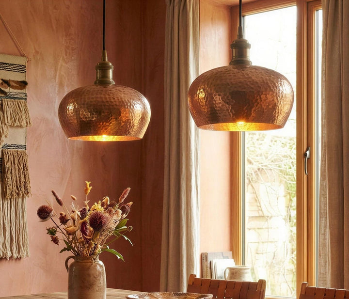 Two copper pendant lights hanging above a dining table with a vase of flowers.