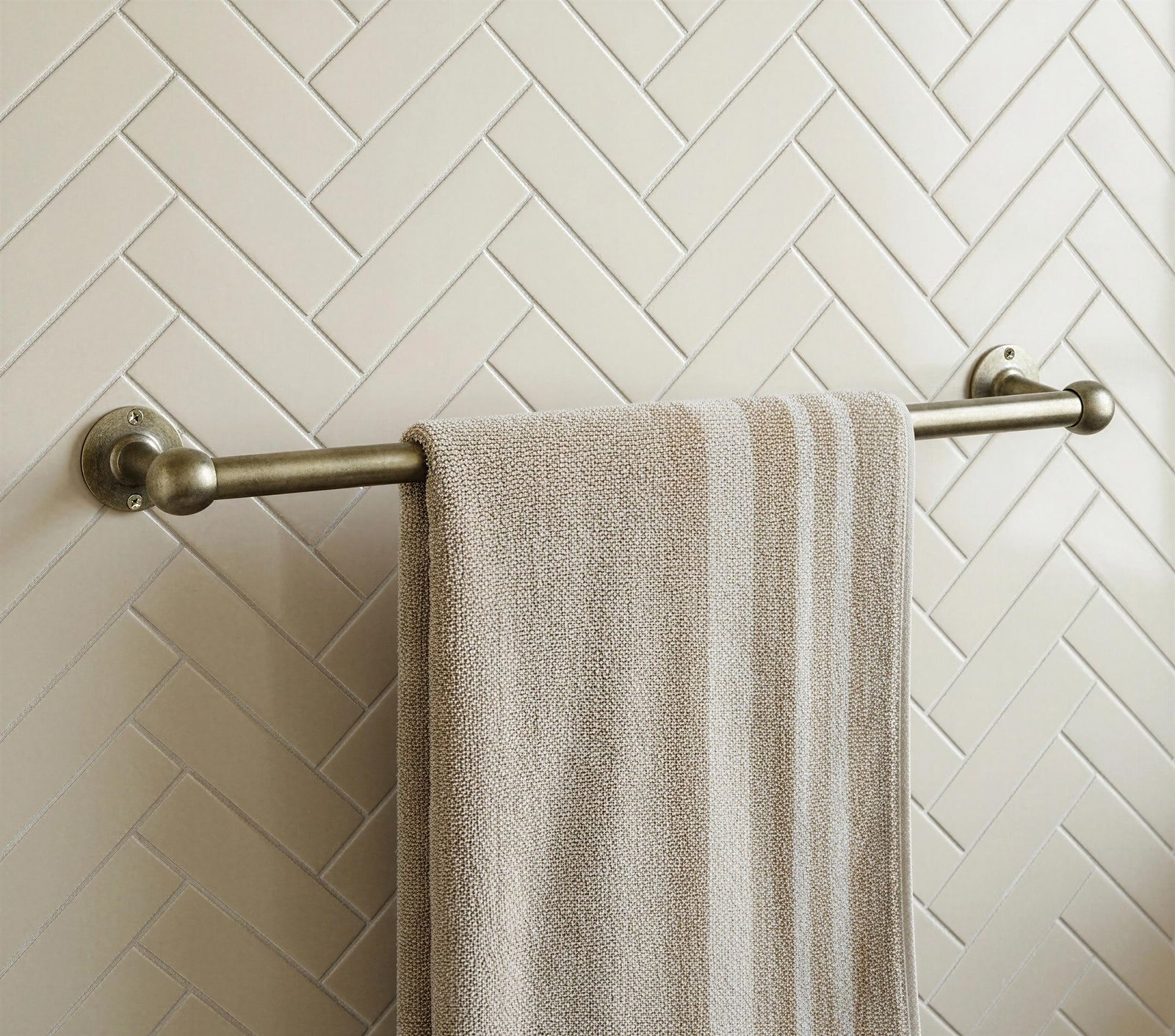 Towel hanging on a towel rack against a tiled wall with a herringbone pattern.