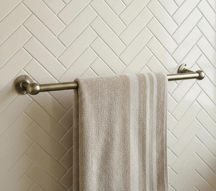 Towel hanging on a towel rack against a tiled wall with a herringbone pattern.