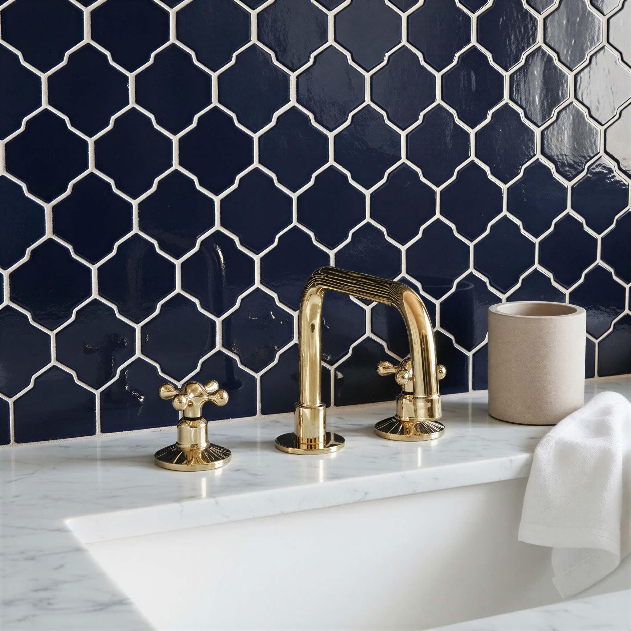 Bathroom sink with gold faucet against a navy blue tiled wall