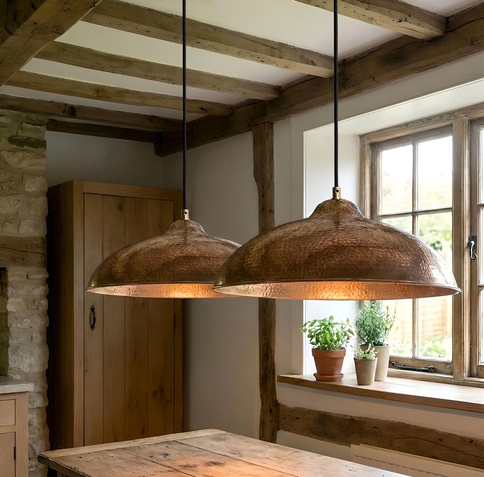 Two rustic pendant lights hanging above a wooden table in a room with stone walls and a window.