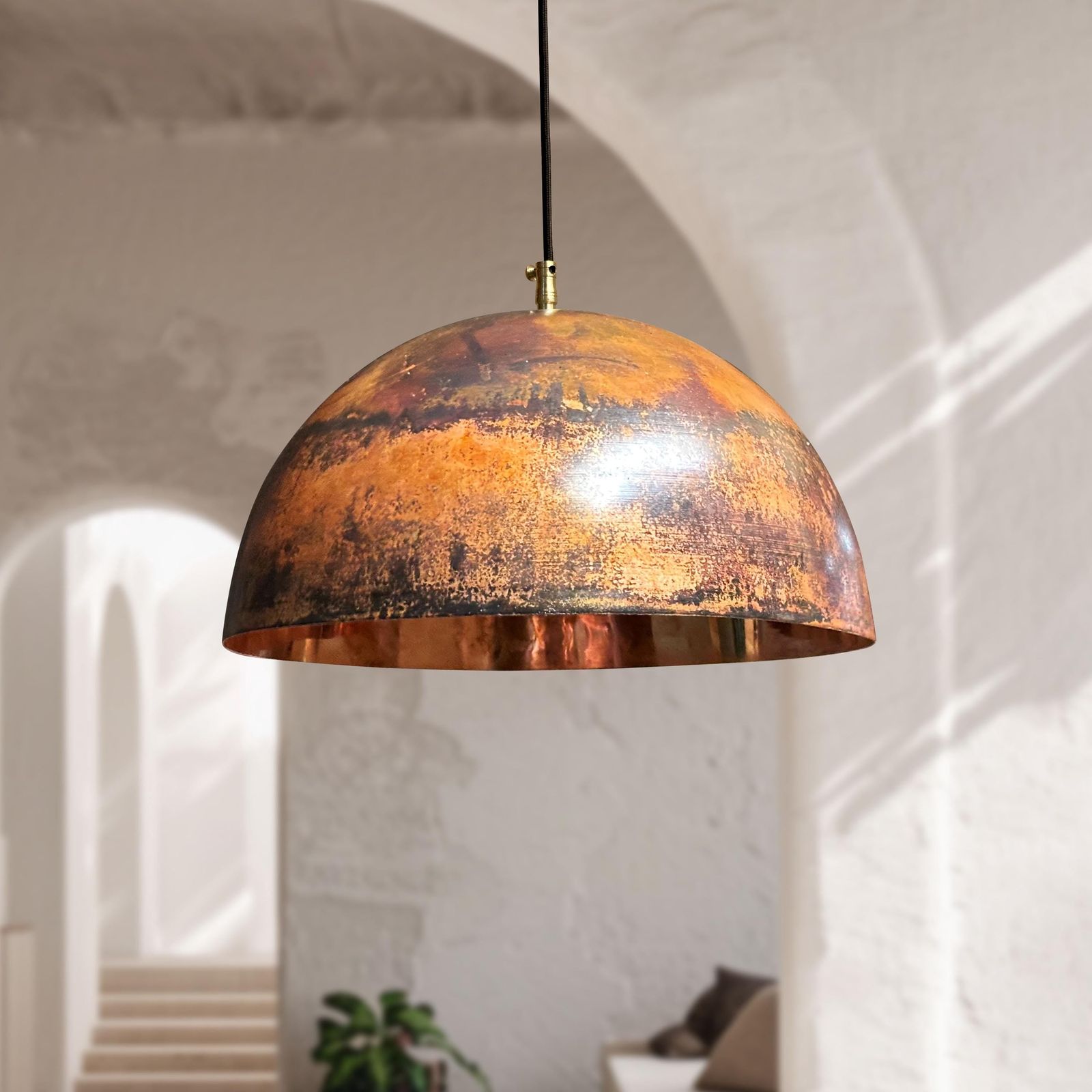 aged copper pendant light hanging in a room with white walls and a plant.