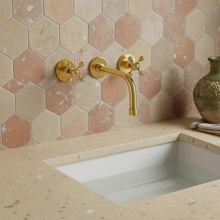 Gold faucet on a tiled wall with a sink below