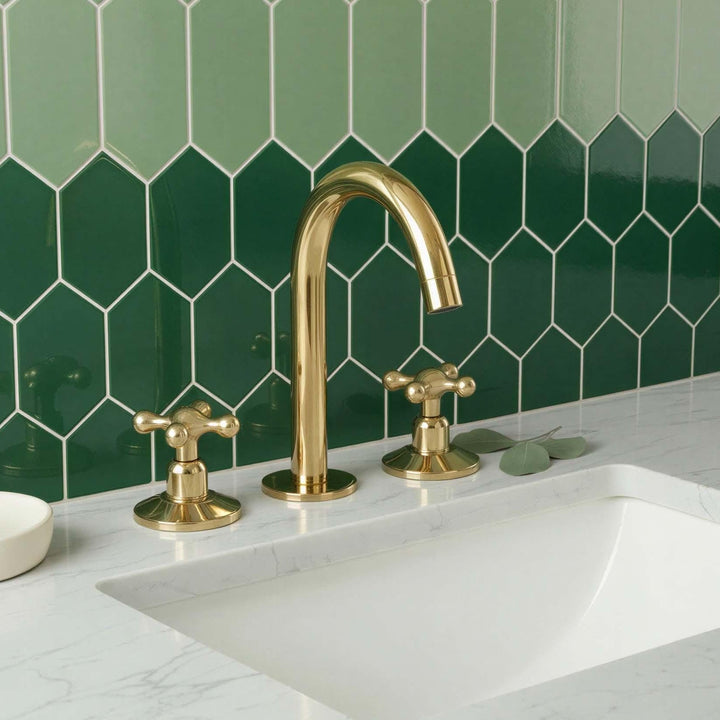 Gold faucet and handles on a white sink with green tiled wall