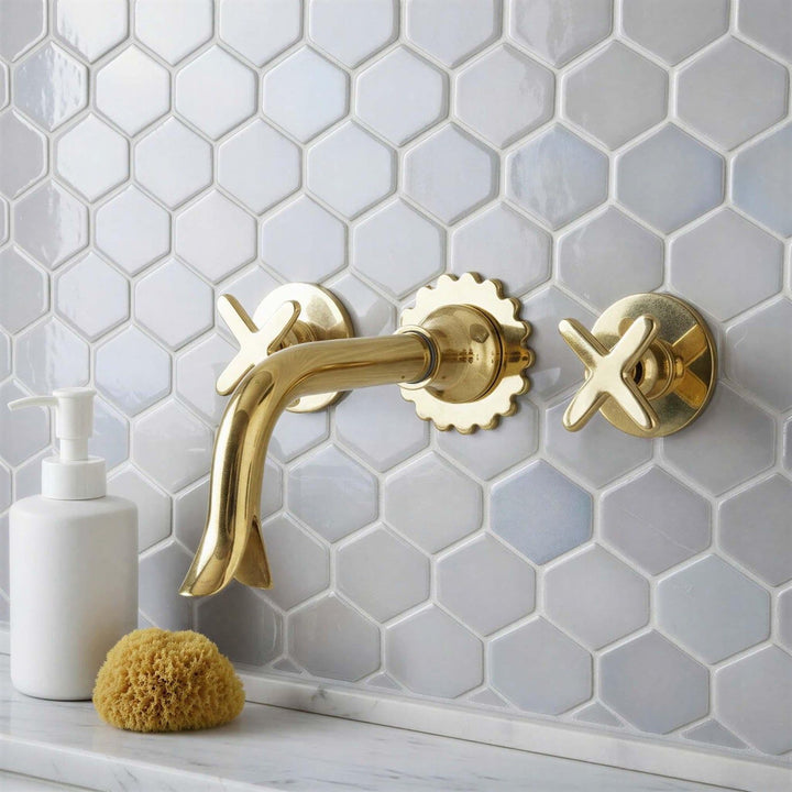 Gold faucet and handles on a hexagonal tiled wall with a white soap dispenser and sponge.