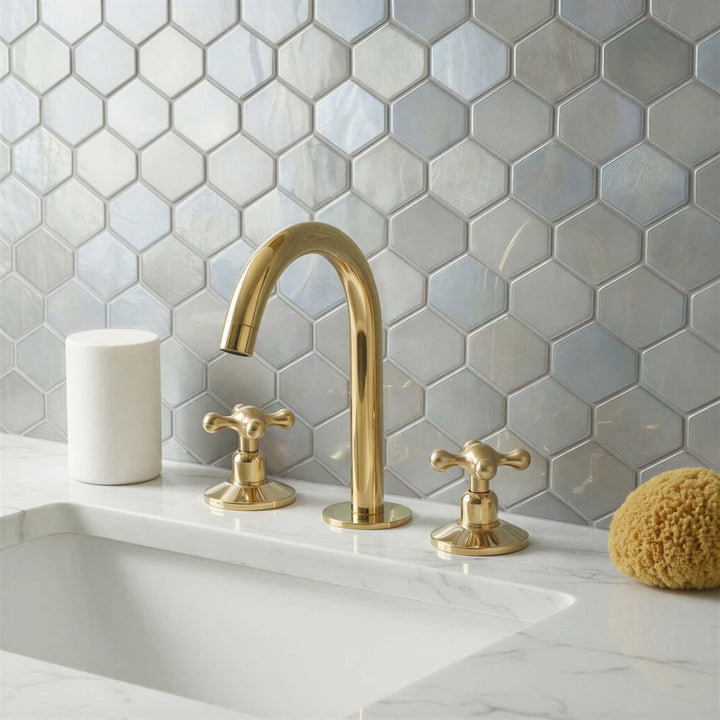 Gold faucet and handles on a white sink with hexagonal gray tiles in the background