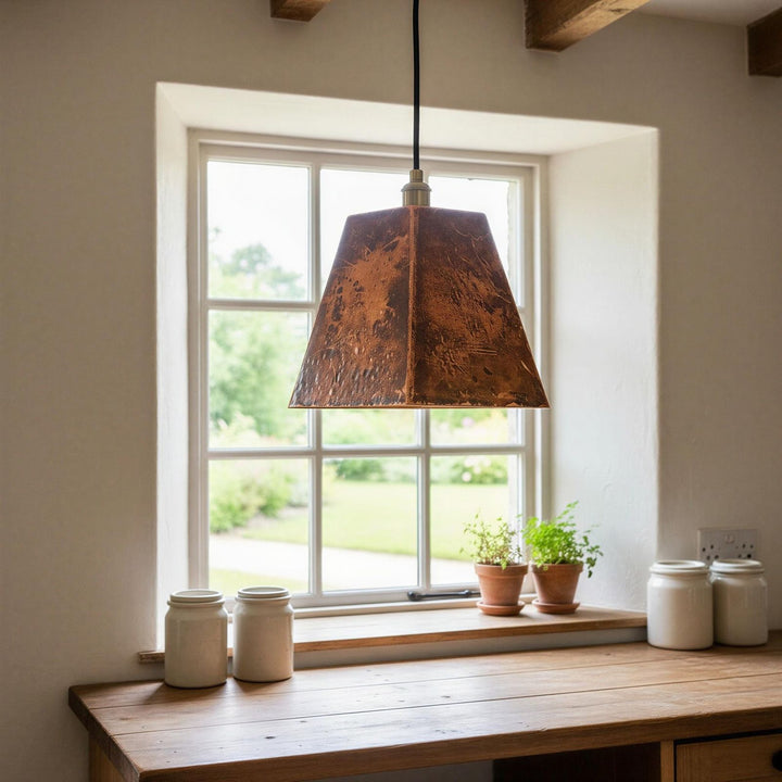 Copper pendant light hanging above a wooden table with jars and plants near a window.
