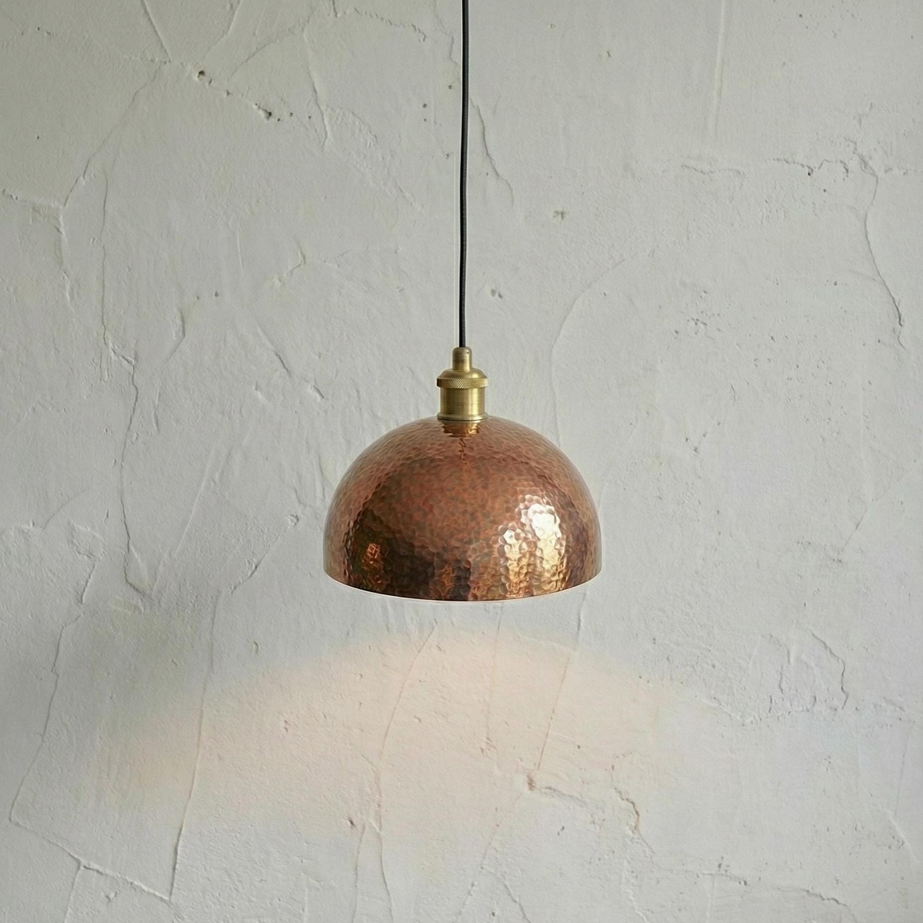 Copper pendant light hanging against a textured white wall