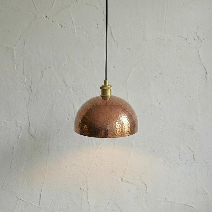 Copper pendant light hanging against a textured white wall
