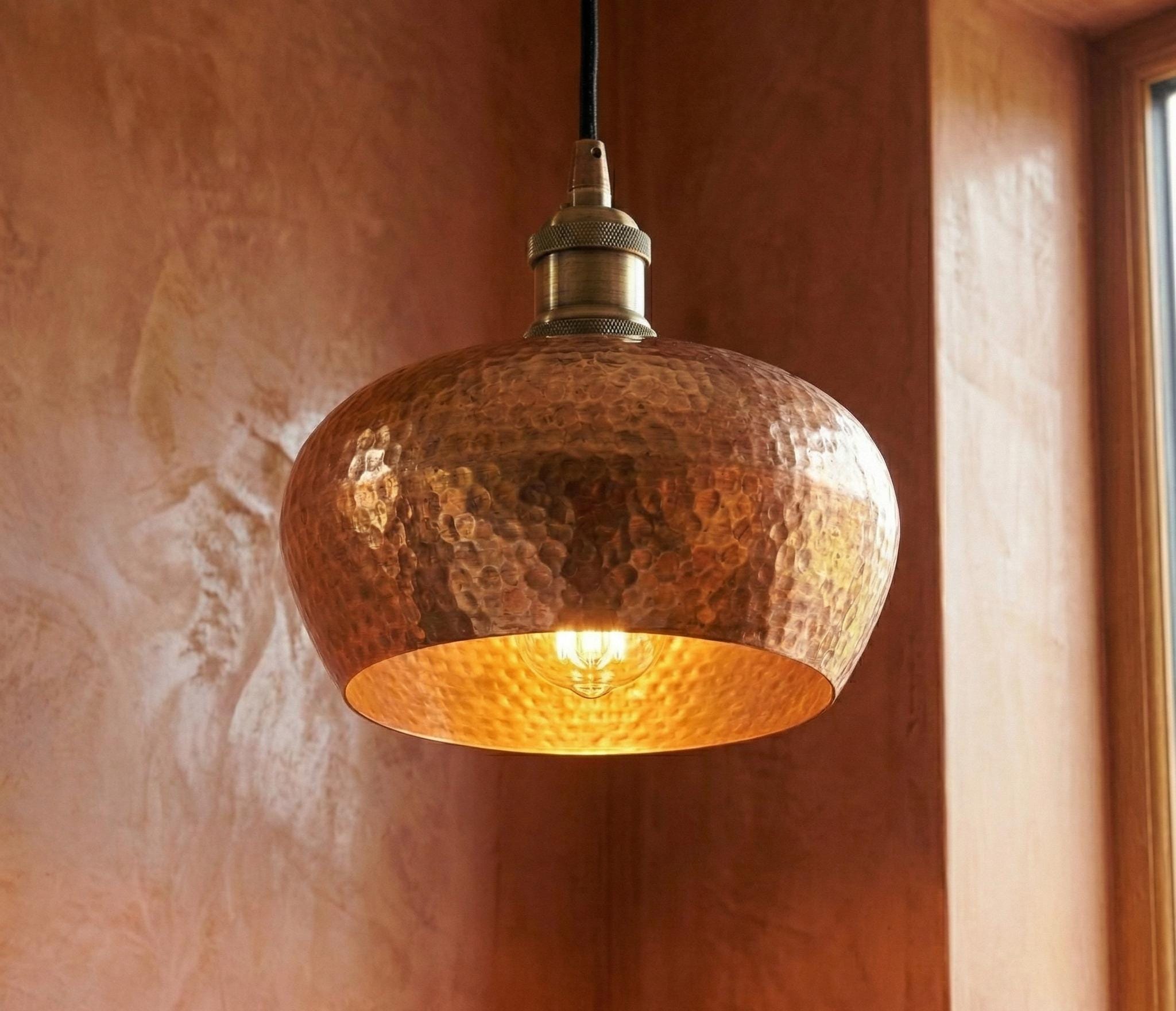 Copper pendant light hanging against a textured wall.