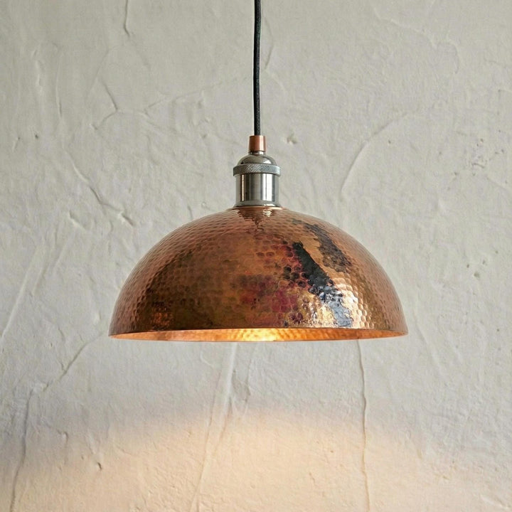 Copper pendant light hanging against a textured white wall
