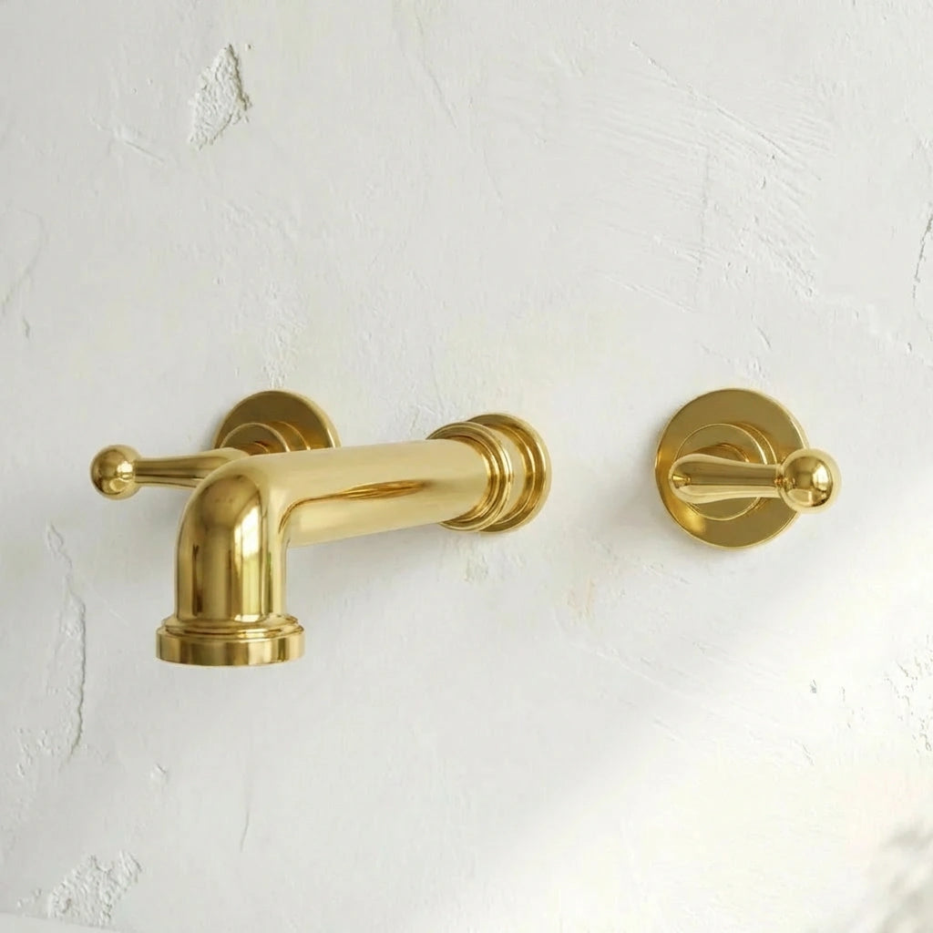 A polished brass wall-mounted bathtub faucet and matching control handle set mounted on a textured white plaster wall.