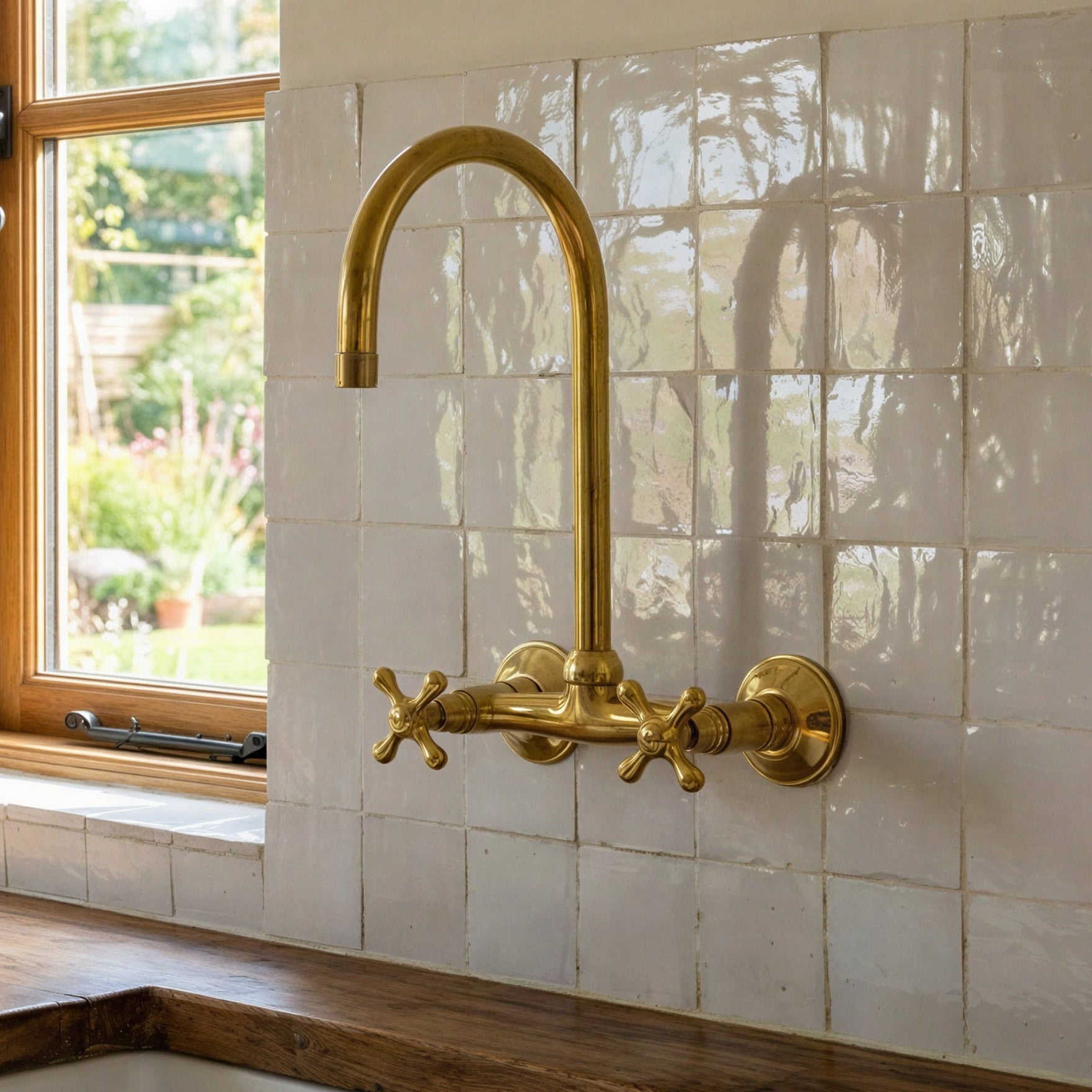 A rustic kitchen scene featuring a tall, curved brass faucet mounted on a white tiled backsplash above a wooden countertop and sink.