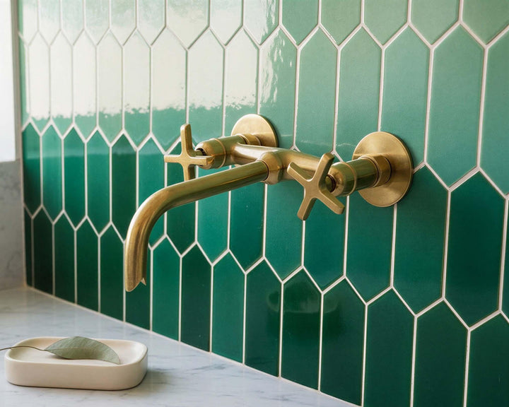 Gold faucet on a green tiled wall with a soap dish below.