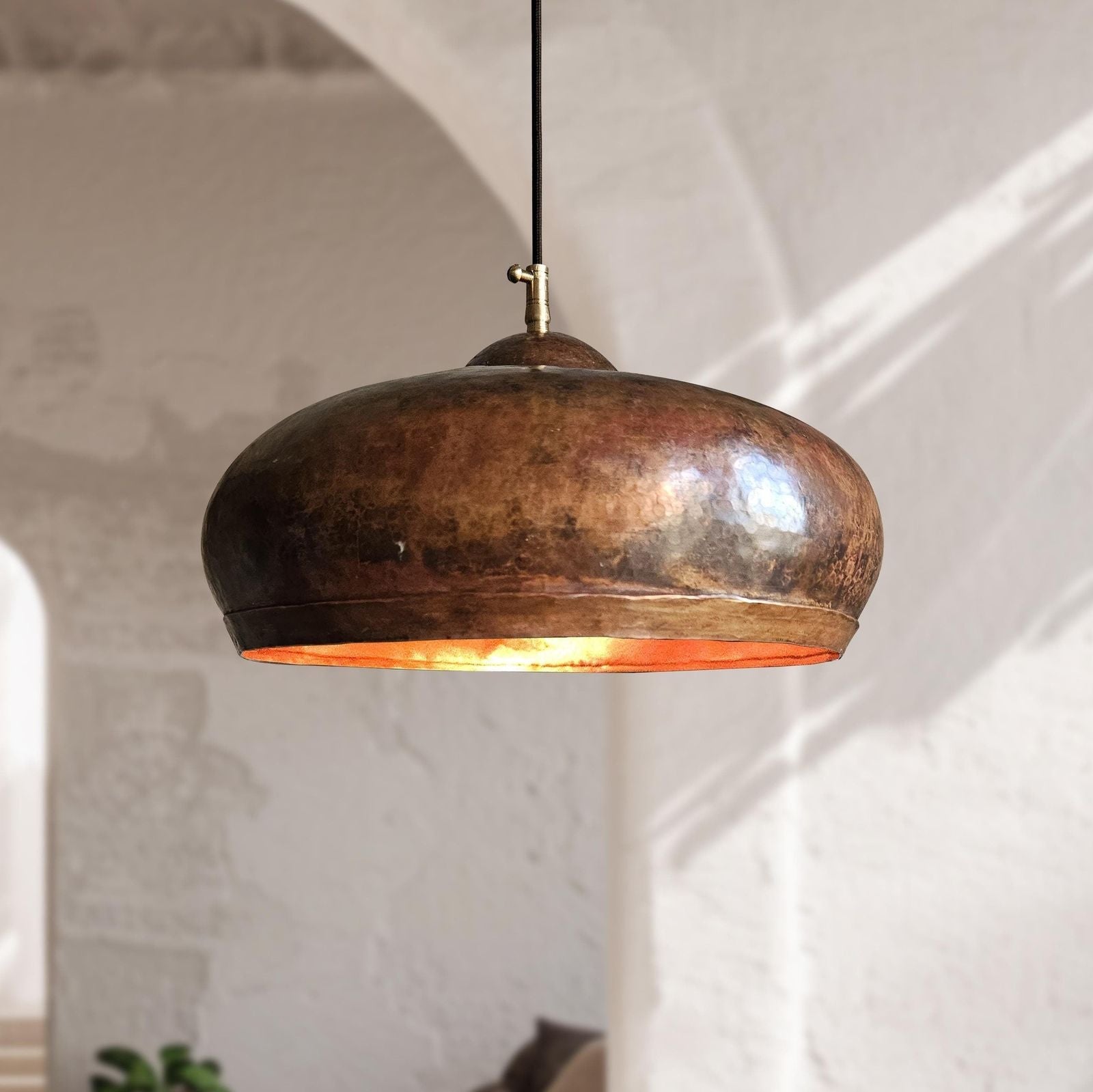 Bronze pendant light hanging against a white wall with natural light.