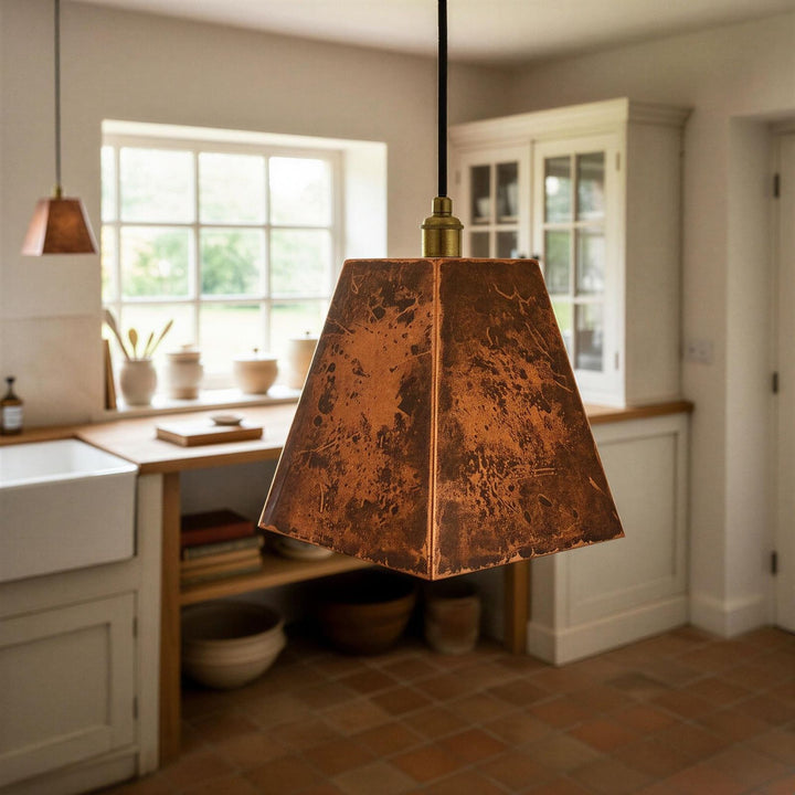 Rustic pendant light hanging in a kitchen with a window and cabinets in the background.