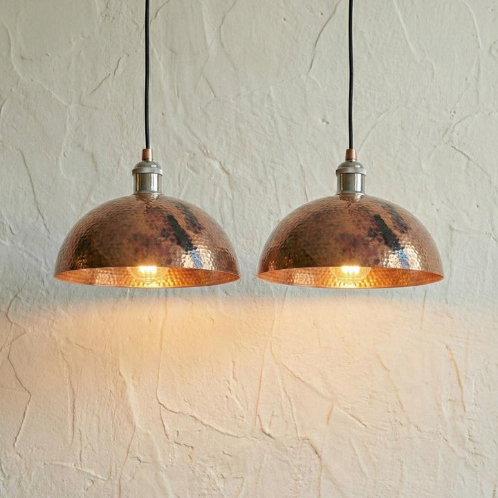 Two copper pendant lights hanging against a textured white wall.